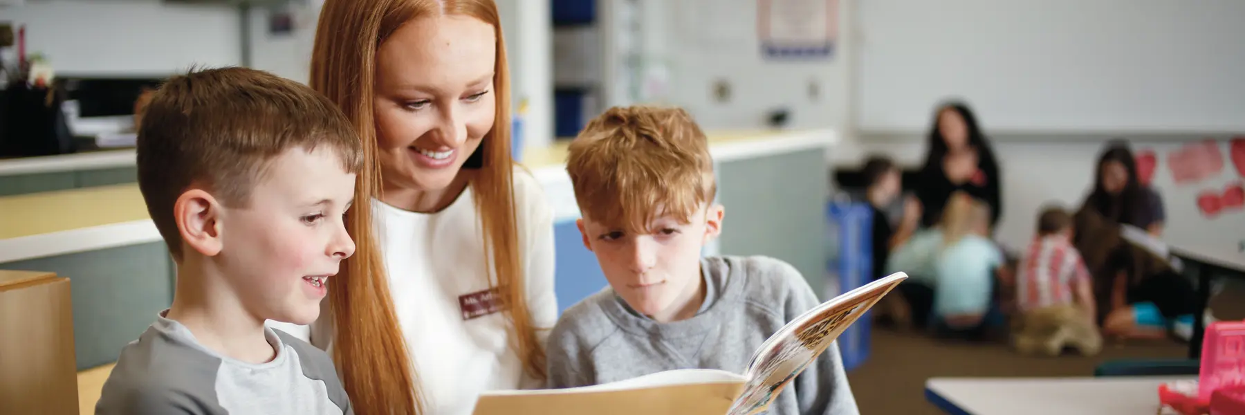 A female teacher reads a book to two young male students