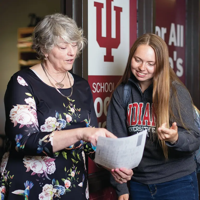 A female professor points to sheet of paper, showing a female student a class schedule