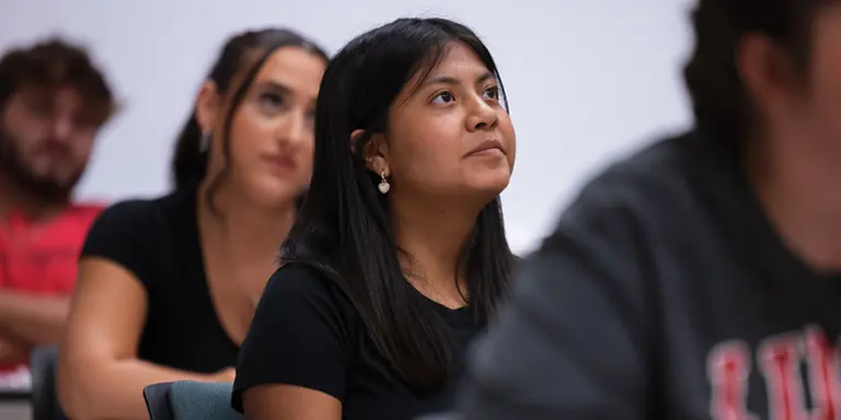 A hopeful-eyed female student gazes at the lecturer (off camera) seated at her desk