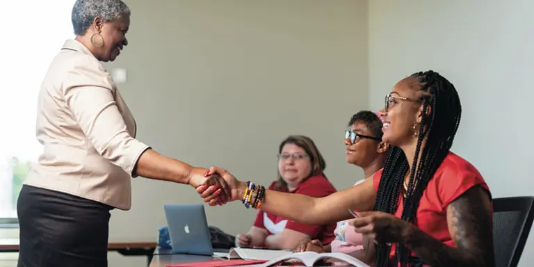 A female professor stands and shakes the hand of a seated female School of Social Work student