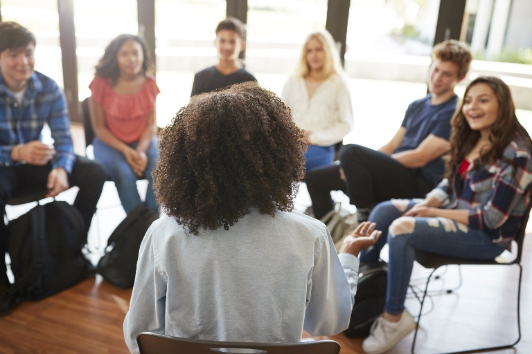 Adult woman mentor sitting in a circle with several high school students.